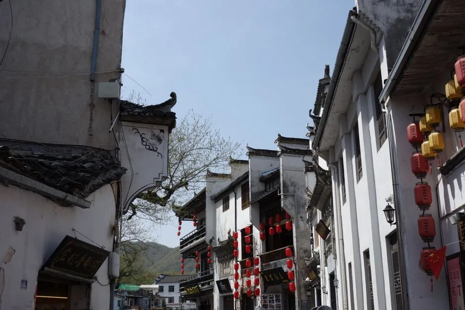 Quaint street in traditional Chinese architecture with red lanterns under a clear blue sky.