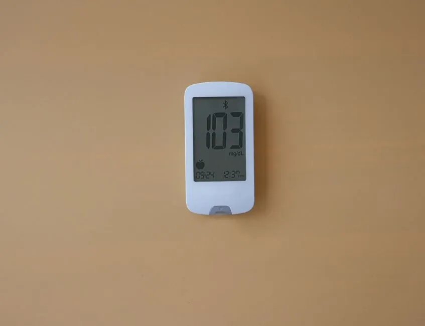 A digital glucose meter displaying blood sugar level on a beige background, ideal for healthcare themes.