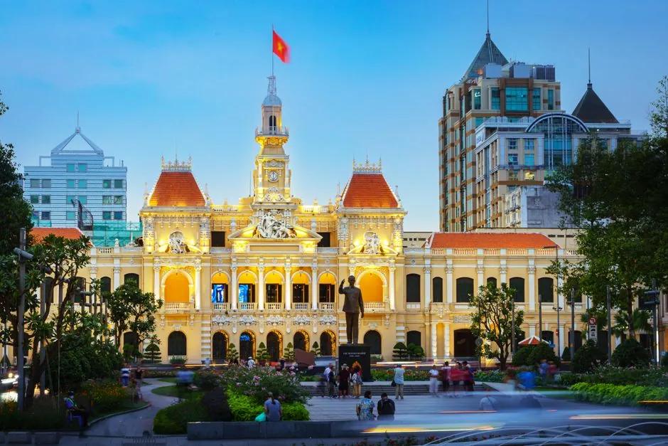 Illuminated People's Committee Building in Ho Chi Minh City at twilight showcasing French colonial architecture.