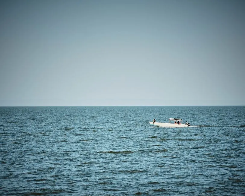 A boat with passengers cruising on the calm waters of Lake Victoria in Kenya under a clear blue sky.